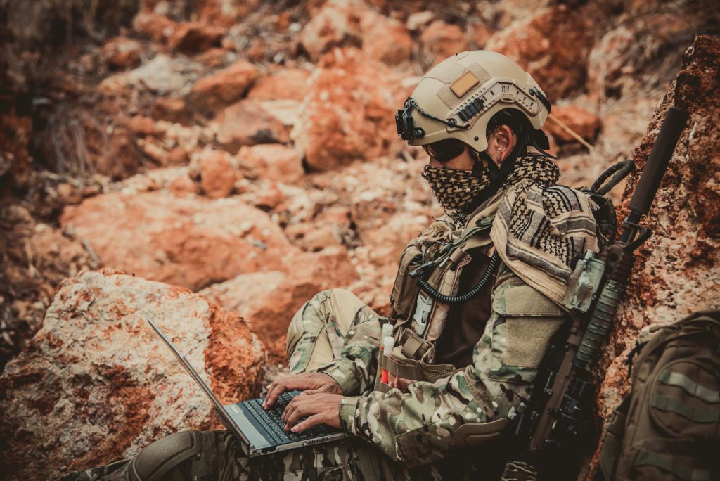 Soldier sitting on rocky surface using a laptop