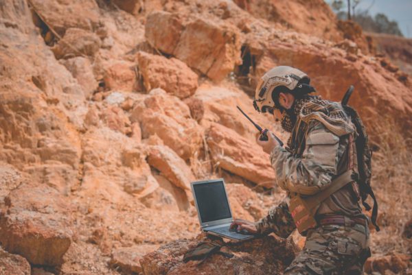 Soldier standing using laptop on rocky surface